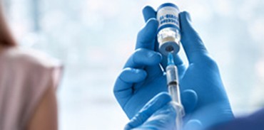 Blue gloved hands withdrawing vaccine from a vial using a syringe